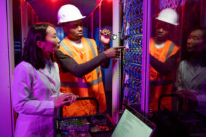 African American workman in hardhat repairing server and explaining reason of server breakdown in data center