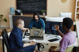 Young African American male IT engineer explaining something to female colleague with cup of coffee sitting next to him at working meeting